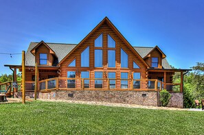 A large log cabin with multiple large windows, a stone foundation, and a wooden deck.