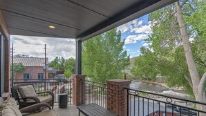 A covered outdoor area with wicker furniture, a brick pillar, and a view of a river. - Best location in Salida! 2 River front decks, looks over Arkansas River waterpark! (Salida)