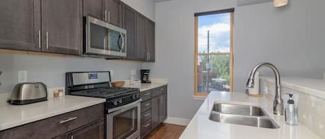 Enjoy cooking in this well-lit kitchen with a large window offering a view of the outdoors, featuring a sink, stove, and oven.