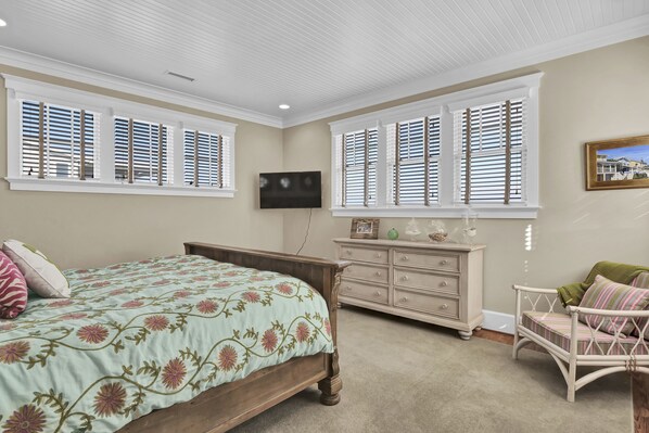 A bedroom with a bed, dresser, chair, and large windows with shutters. - Fonvielle–Exceptional upscale and spacious oceanfront home w/ gourmet kitchen (Wrightsville Beach)