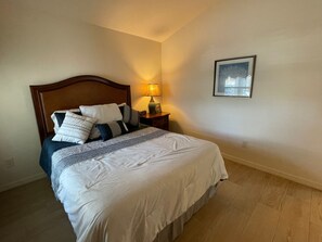 A neatly made bed with a wooden headboard, a bedside table with a lamp, and a framed picture on the wall. - Your Private Slice of Paradise Near Brownwood! (The Villages)