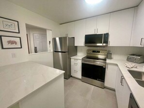 A modern kitchen with stainless steel appliances, white cabinetry, and a tiled floor.