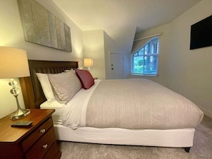 A bedroom with a bed, bedside table, lamp, and a window with blinds.