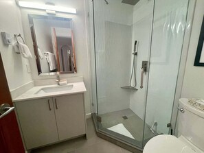 A modern bathroom with a glass-enclosed shower, a white sink with a mirror above, and a toilet with a white tank.
