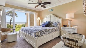 A bedroom with a bed, a nightstand, a lamp, a chair, a suitcase, and a view of the beach. - Shorewood 312 -  3 bedroom Beautiful Ocean Front (Hilton Head Island)