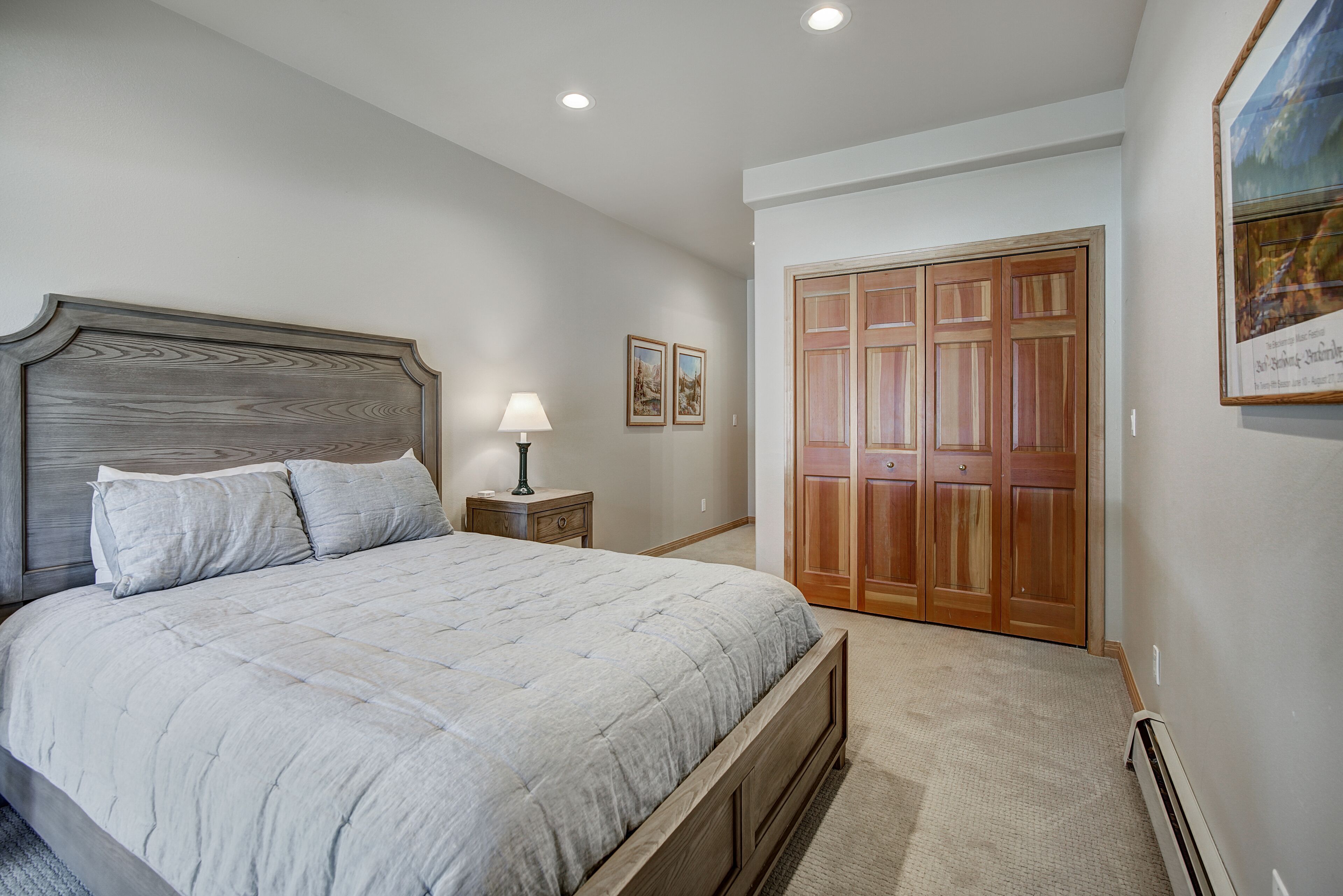 A bedroom with a large bed, a nightstand, a lamp, and a wooden wardrobe.