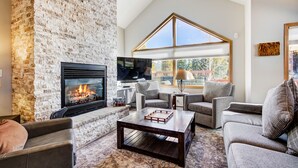 A living room with a stone fireplace, comfortable seating, and large windows. - RENOVATED! Ski In/Out Townhome Private Hot Tub w/ Panoramic VIEWS! PINE97 (Breckenridge)