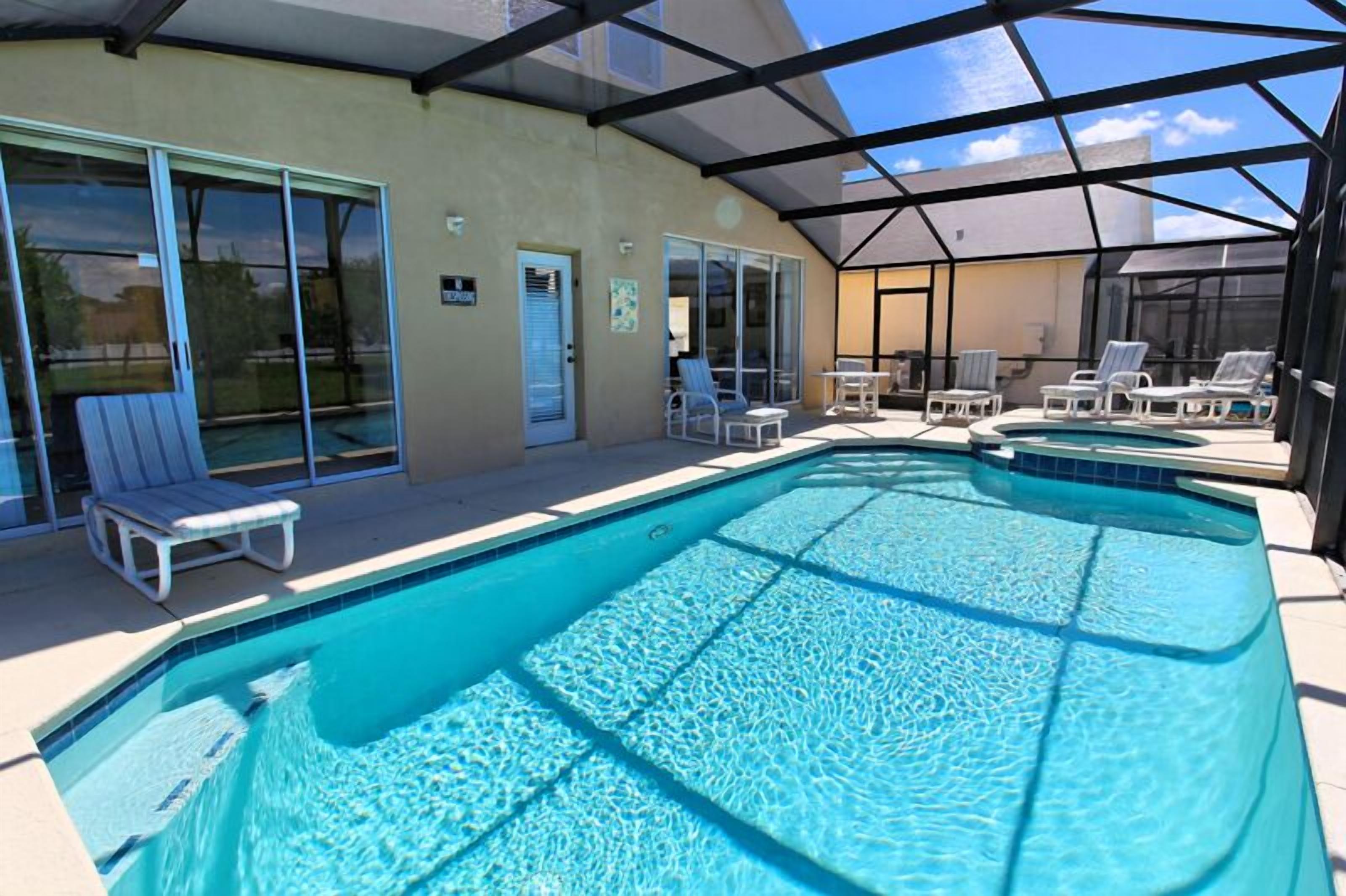 A covered outdoor swimming pool with lounge chairs and a glass door entrance.