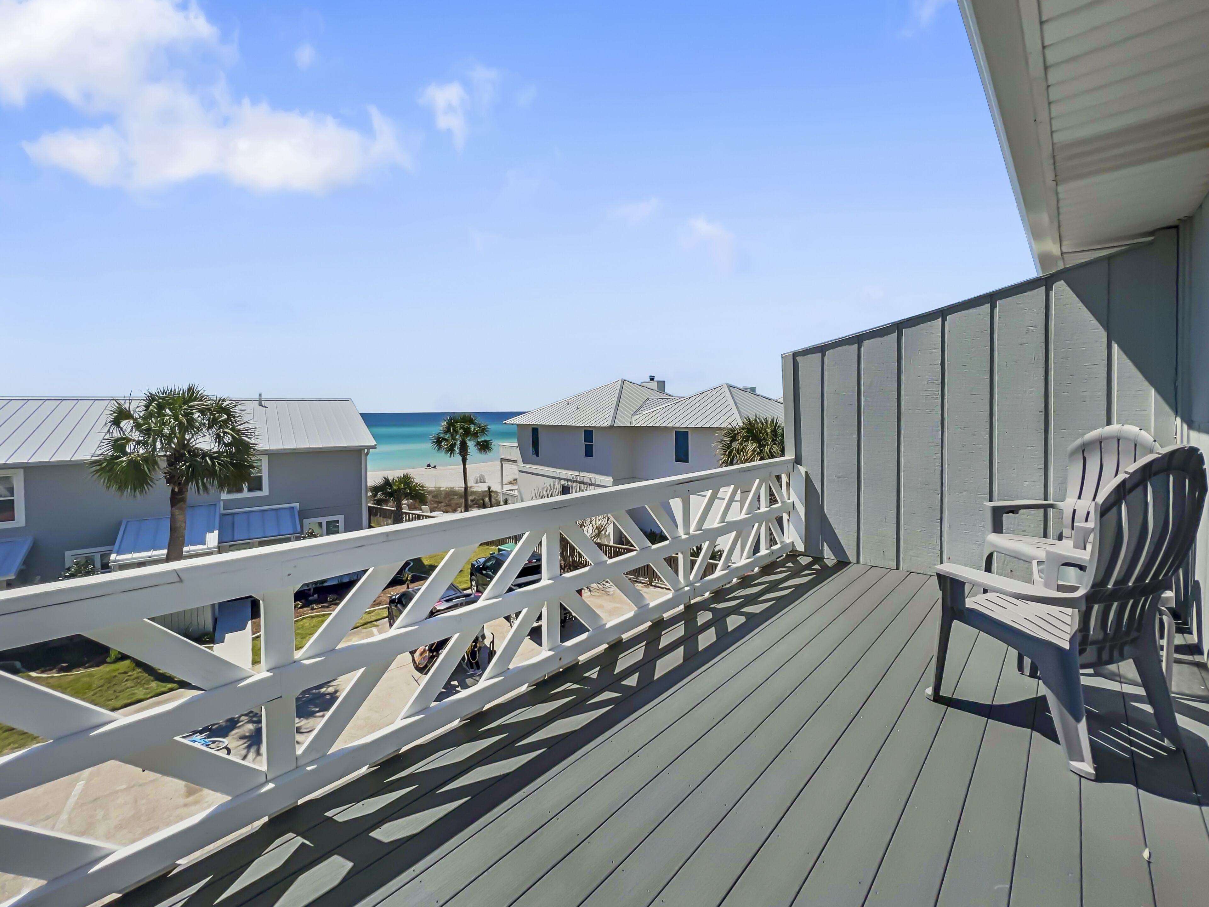 Eine Holzterrasse mit weißer Reling, einem weißen Stuhl und Blick auf Strand und Meer.