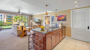 A modern kitchen with a central island, a dining area with a sofa and table, and a view of a building with balconies.