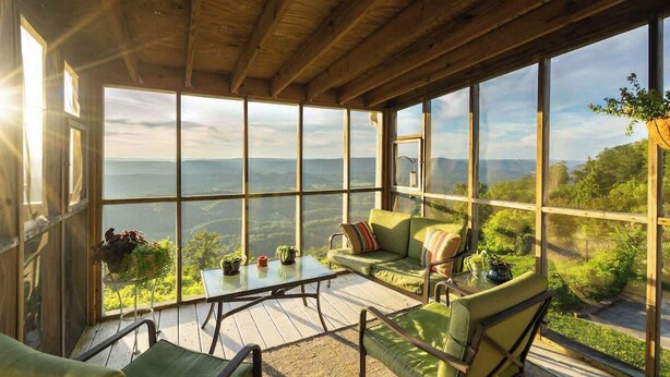 A spacious room with large windows, a wooden ceiling, and a green sofa with cushions.
