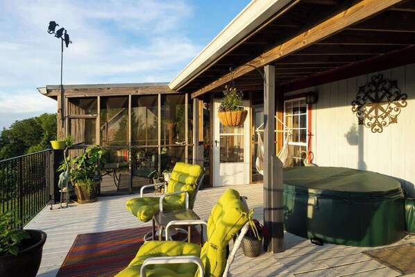 A covered deck with outdoor seating, a hot tub, and potted plants.