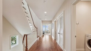 Un couloir doté d’un plancher en bois, un escalier avec une rampe en bois et une porte avec une fenêtre.