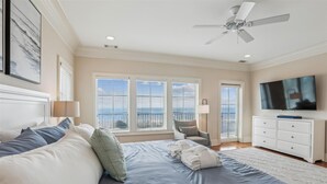 Une chambre à coucher avec un lit, une chaise, une télévision et un balcon avec des fenêtres.