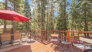 A wooden deck with outdoor furniture, including chairs and a table, surrounded by a metal railing.