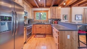 A modern kitchen with wooden cabinets, stainless steel appliances, and a large window providing natural light.