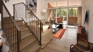 A spacious living area with a wooden staircase, a sofa set, a coffee table, and a view through large windows. - Large Ski-In/Out Lionshead Condo w/ Private Hot Tub and Best Vail Slope Views (Vail)