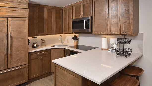 A kitchen with wooden cabinets, a stainless steel microwave, a sink, and a bar area with stools. - Large Ski-In/Out Lionshead Condo w/ Private Hot Tub and Best Vail Slope Views (Vail)