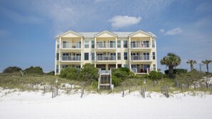 A multi-story hotel with balconies, located on a beach with a sandy foreground and a clear sky.