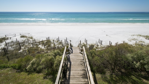 A wooden boardwalk leading to a sandy beach with a clear view of the ocean.