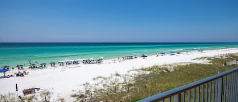 A beach with a wooden deck and a railing, overlooking a sandy beach with umbrellas and beach chairs.