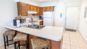 A kitchen with wooden cabinets, a white countertop, a sink, and two bar stools with woven seats.