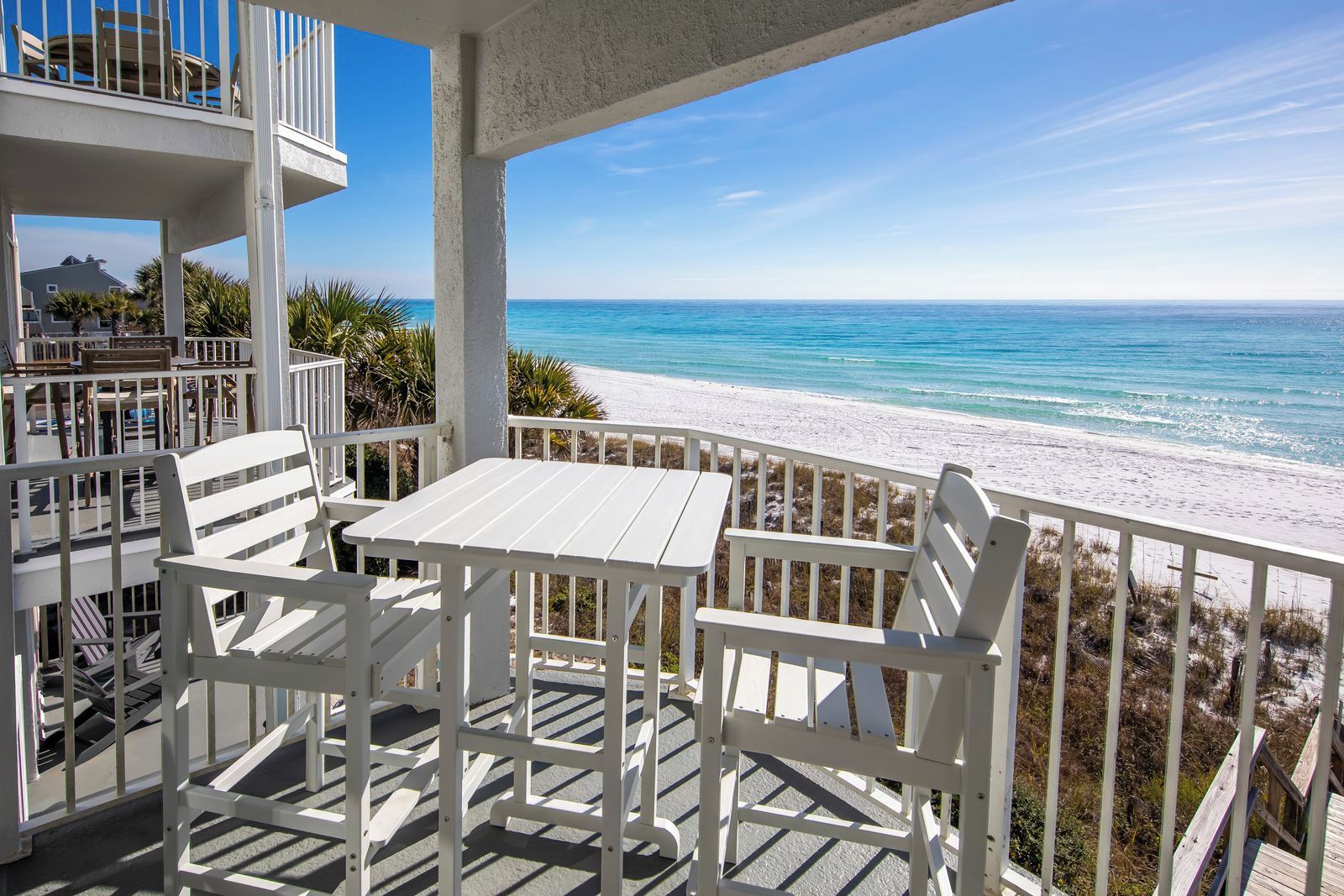 A balcony with white furniture overlooking a beach.