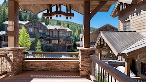 A wooden deck with stone walls and a view of a large lodge with multiple buildings and a mountain backdrop. - Base Camp 480 | Mountain Townhome | On The Slopes | Private Hot Tub (Winter Park)