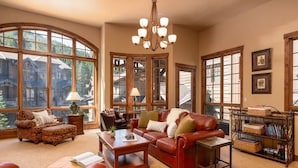 A spacious living room with large windows, a fireplace, leather sofas, and a bookshelf. - Base Camp 480 | Mountain Townhome | On The Slopes | Private Hot Tub (Winter Park)