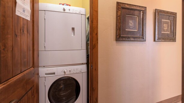 A laundry room with stacked washers and dryers, wooden cabinets, and framed pictures on the wall. - Base Camp 480 | Mountain Townhome | On The Slopes | Private Hot Tub (Winter Park)