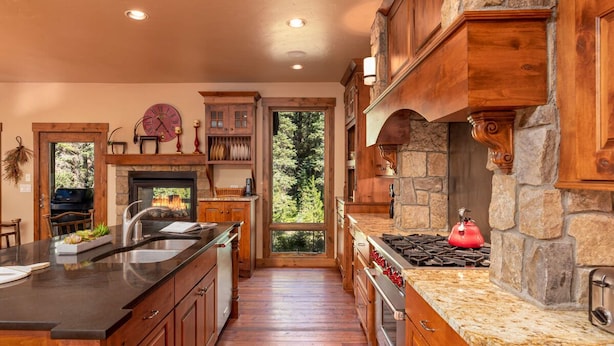A spacious kitchen with a large island, stone accents, and a view of the outdoors. - Base Camp 480 | Mountain Townhome | On The Slopes | Private Hot Tub (Winter Park)