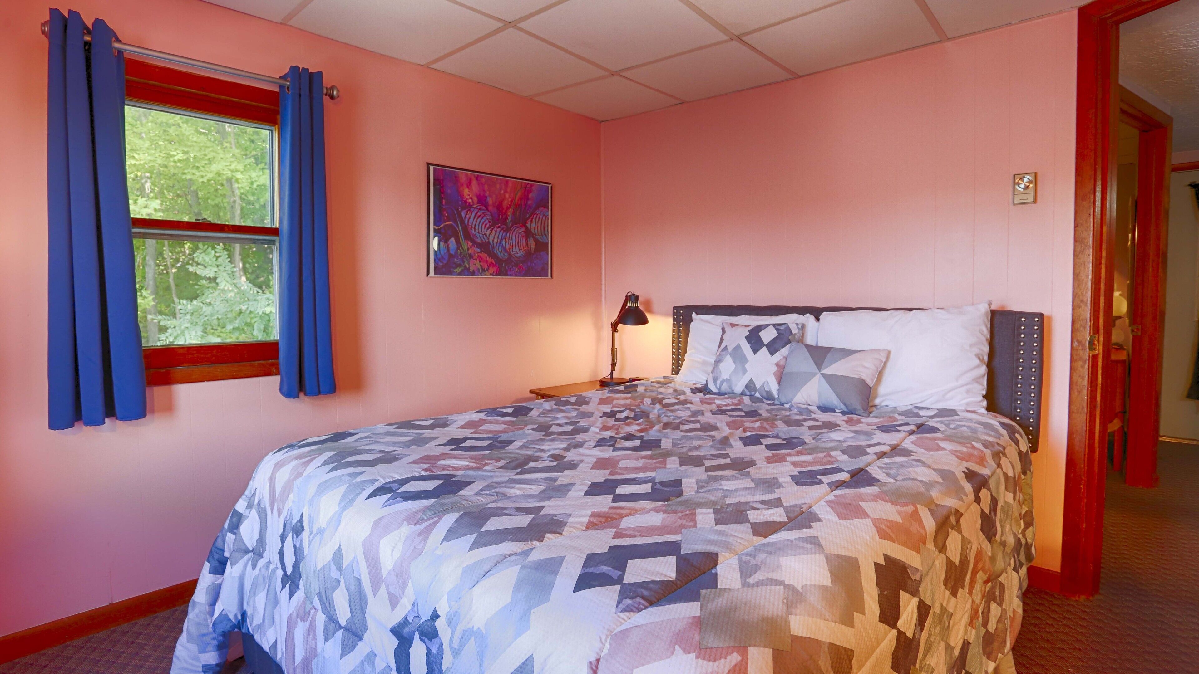 Een slaapkamer met een bed, gordijnen voor het raam, een nachtkastje en een schilderij aan de muur.