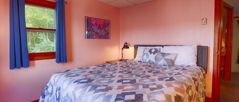 Een slaapkamer met een bed, gordijnen voor het raam, een nachtkastje en een schilderij aan de muur.