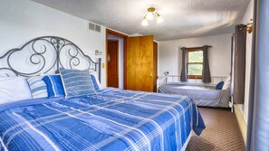 A bedroom with a large bed, a smaller bed, a window with curtains, and a door. - Bluestone Cottage: Sit back, Relax, and Enjoy Breathtaking Sunsets! (Keuka Park)