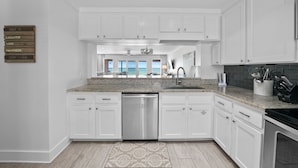 A modern kitchen with white cabinetry, a stainless steel dishwasher, and a granite countertop.