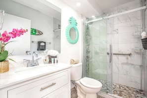 A modern bathroom with a glass shower enclosure, a white toilet, and a vanity with a mirror and sink.