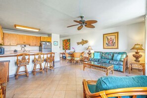 A spacious living area with a sofa, chairs, a dining table, and a kitchen area with wooden cabinets and a refrigerator.