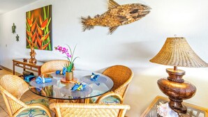Un comedor con sillas de mimbre, una mesa de vidrio y un colgador decorativo con forma de pez.