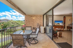 Ein Balkon mit Glastisch und Stühlen, einer Steinwand, einem Fernseher und einem Holzschrank.