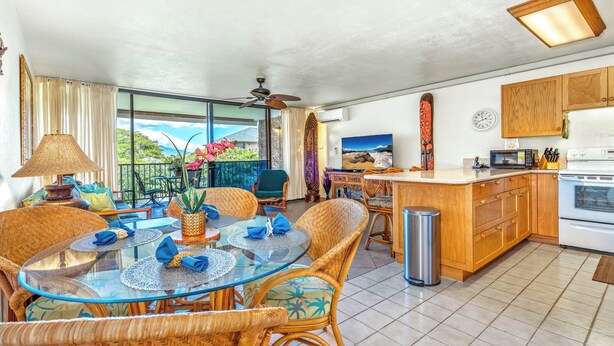 Amplia sala de estar con una mesa de comedor de cristal rodeada de sillas de mimbre, una cocina con armarios de madera y un ventanal con vistas al exterior.