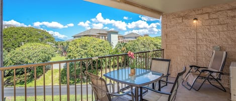 A balcony with a glass table and chairs, a stone wall, and a view of a residential area.