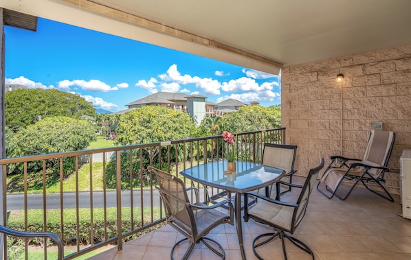 A balcony with a glass table and chairs, a stone wall, and a view of a residential area.