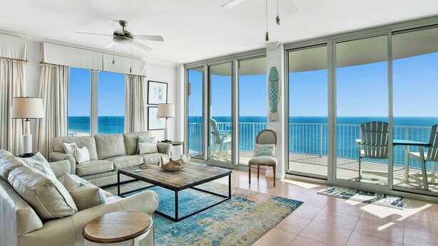 A spacious living room with a large sofa, a coffee table, and a view of the ocean through large sliding glass doors.