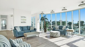 A spacious living room with a large window, a sofa, a coffee table, and a potted plant.