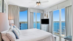 A hotel room with a large bed, a ceiling fan, a TV, and a view of the sea.