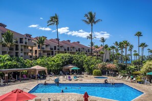 A hotel pool area with multiple swimming pools, lounge chairs, and palm trees.