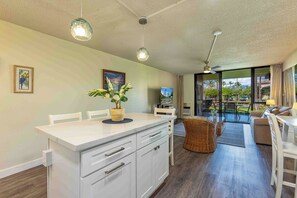 A modern kitchen with white cabinetry, a dining area with a white table and chairs, and a living area with a sofa and a TV.