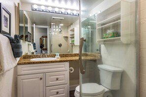 A bathroom with a granite countertop, white vanity, a glass-enclosed shower, and a toilet.