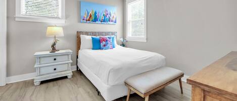 A bedroom with a bed, a nightstand, a lamp, a bench, and a painting on the wall.