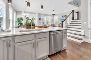 A modern kitchen with a large island, stainless steel dishwasher, and a wooden bowl centerpiece.